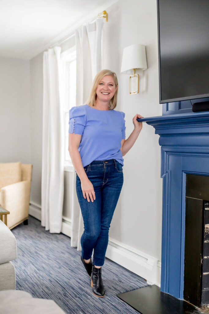 Lori Fischer of Rethink Home Interiors standing by fireplace of staged home