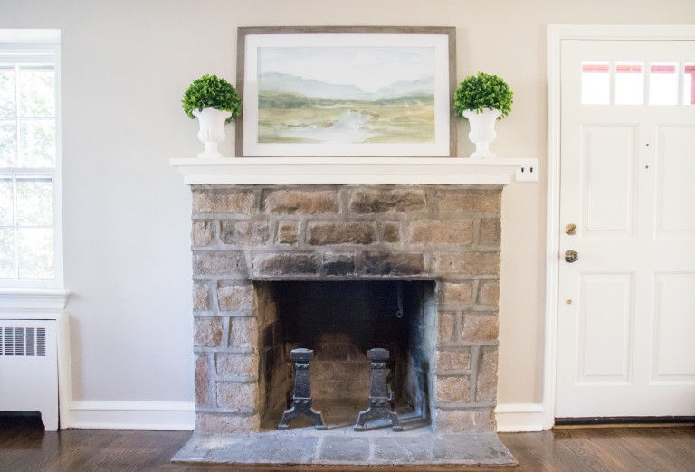 fireplace with plants and a painting on the mantel